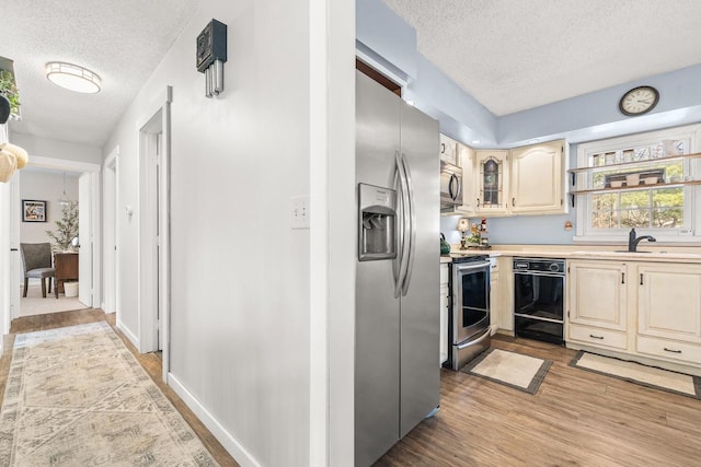 kitchen with light wood-style flooring, a sink, a textured ceiling, appliances with stainless steel finishes, and light countertops