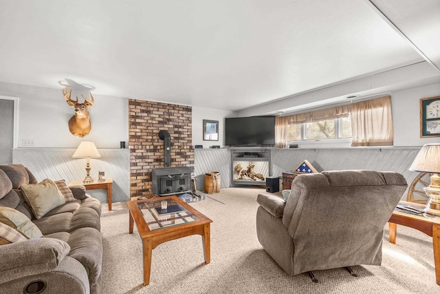 carpeted living area featuring a wood stove and a wainscoted wall