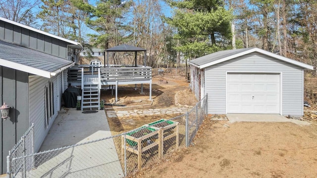 exterior space featuring a detached garage, fence, a wooden deck, an outdoor structure, and driveway