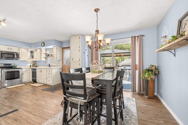 dining area featuring an inviting chandelier, light wood-style flooring, baseboards, and a textured ceiling