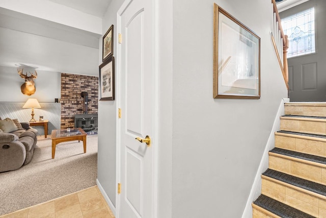 stairway with tile patterned floors, carpet flooring, baseboards, and a wood stove