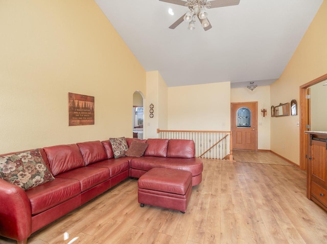 living area featuring arched walkways, light wood-style flooring, high vaulted ceiling, and baseboards