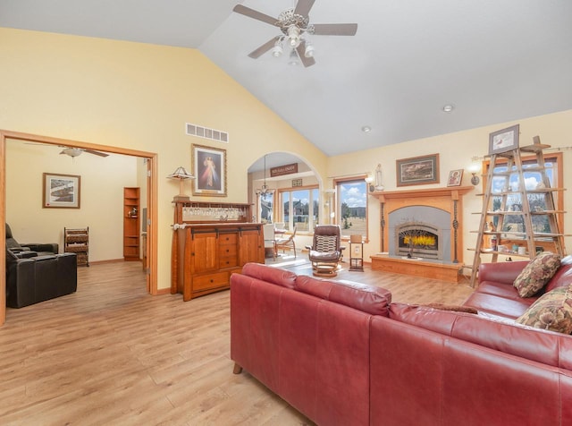 living area with visible vents, high vaulted ceiling, arched walkways, a warm lit fireplace, and light wood-type flooring