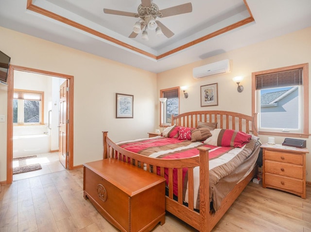 bedroom featuring a tray ceiling, an AC wall unit, light wood finished floors, and connected bathroom