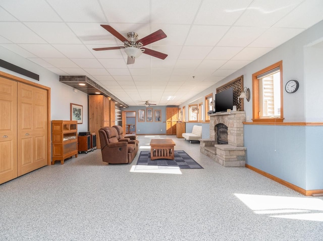 living room featuring a stone fireplace, a paneled ceiling, baseboards, and ceiling fan