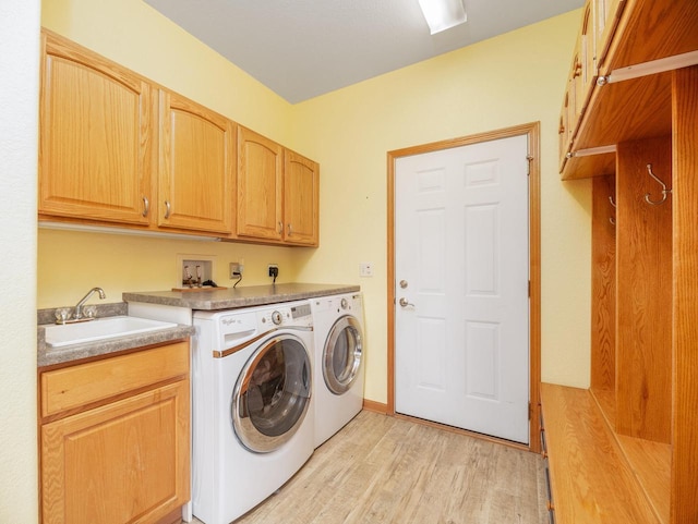 laundry room with cabinet space, washer and dryer, light wood-style flooring, and a sink