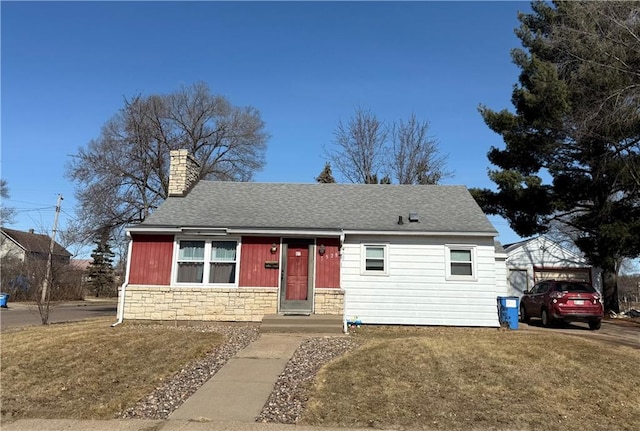 view of front facade featuring a shingled roof, a front yard, stone siding, and a chimney