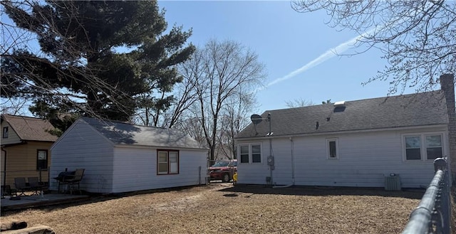 back of house featuring a patio area, an outbuilding, central AC, and a shingled roof