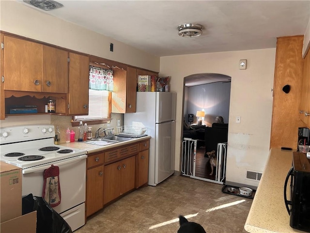 kitchen featuring brown cabinets, white appliances, light countertops, and a sink