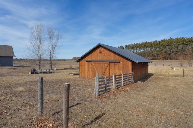 view of outbuilding with a rural view, an outdoor structure, and fence