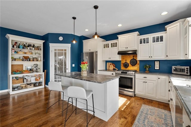 kitchen featuring wood finished floors, a breakfast bar, stainless steel appliances, white cabinets, and under cabinet range hood