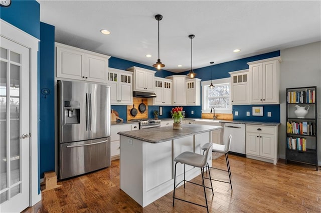 kitchen featuring under cabinet range hood, glass insert cabinets, appliances with stainless steel finishes, and white cabinets