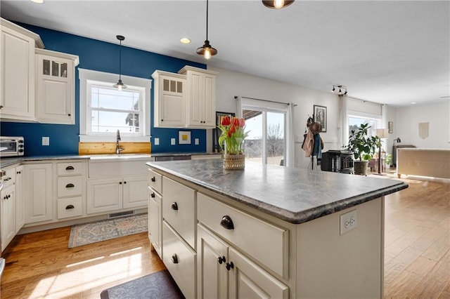 kitchen with a kitchen island, a sink, glass insert cabinets, pendant lighting, and light wood-type flooring