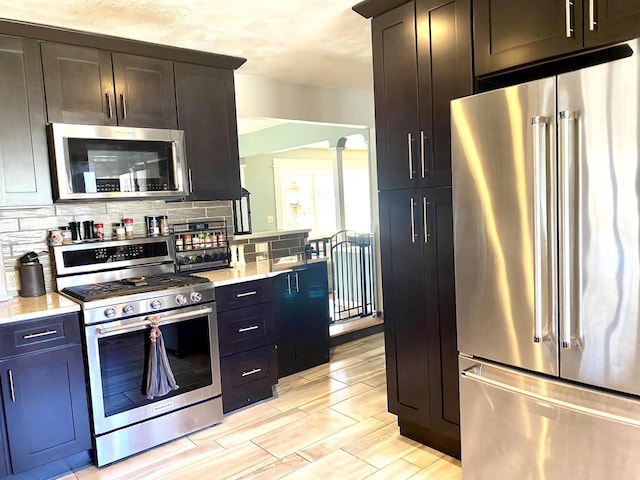 kitchen featuring light stone counters, ornate columns, wood finish floors, stainless steel appliances, and decorative backsplash