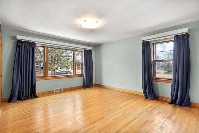 unfurnished room featuring visible vents, plenty of natural light, baseboards, and light wood finished floors