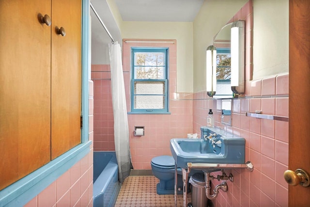 full bathroom featuring a wainscoted wall, toilet, shower / tub combo with curtain, tile walls, and a sink