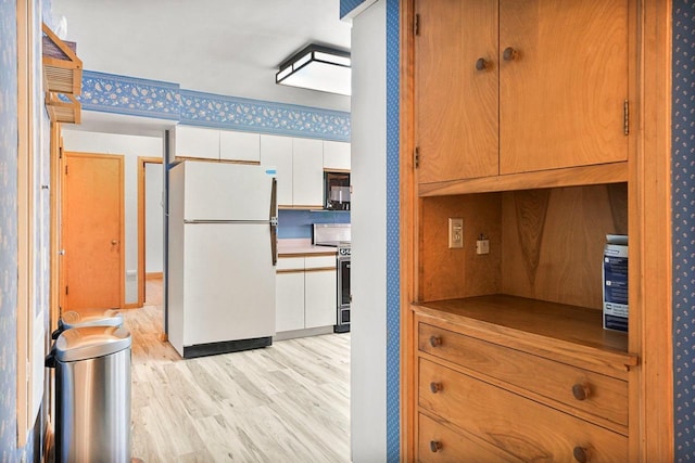 kitchen featuring light wood finished floors, freestanding refrigerator, stainless steel range with electric stovetop, white cabinets, and black microwave