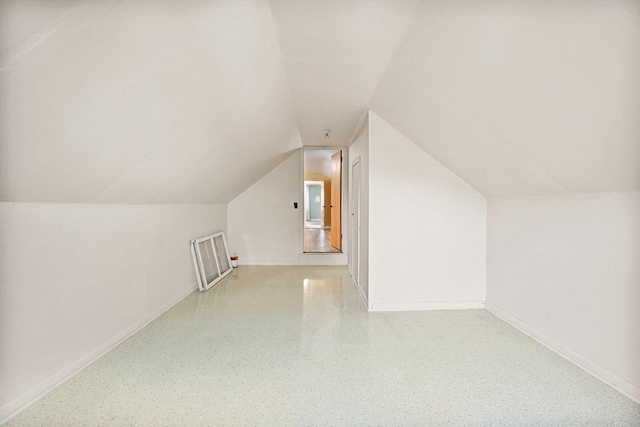 additional living space featuring vaulted ceiling, speckled floor, and baseboards