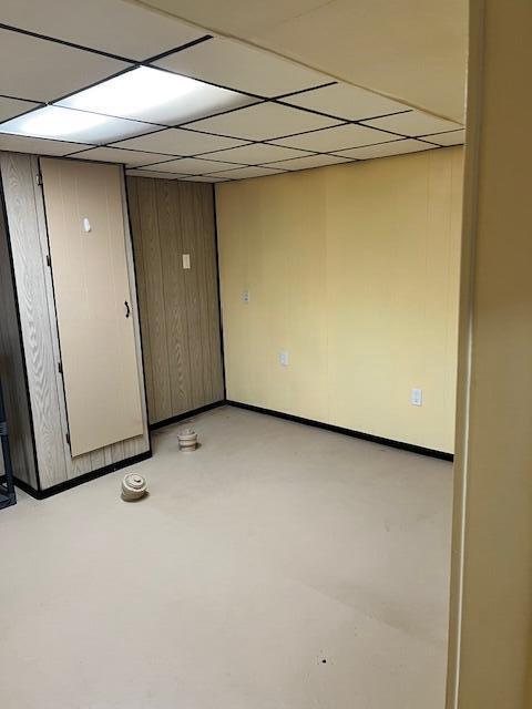 empty room featuring concrete floors, wooden walls, baseboards, and a drop ceiling