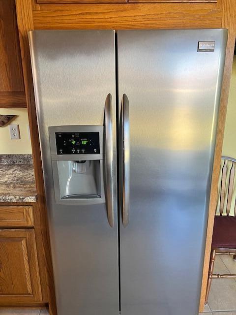 room details with stainless steel fridge, dark stone counters, and brown cabinets