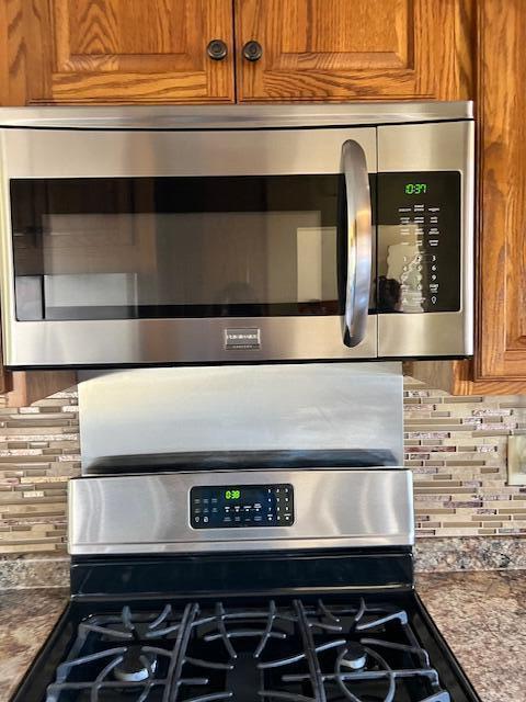 interior details with dark countertops, brown cabinets, backsplash, and appliances with stainless steel finishes