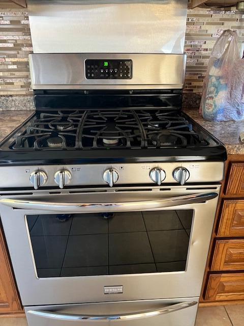 room details featuring gas range, brown cabinets, and backsplash