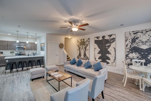 living room featuring light wood finished floors, visible vents, stairway, and ceiling fan