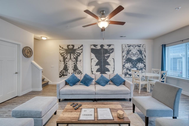 living room featuring stairway, a ceiling fan, visible vents, wood finished floors, and baseboards