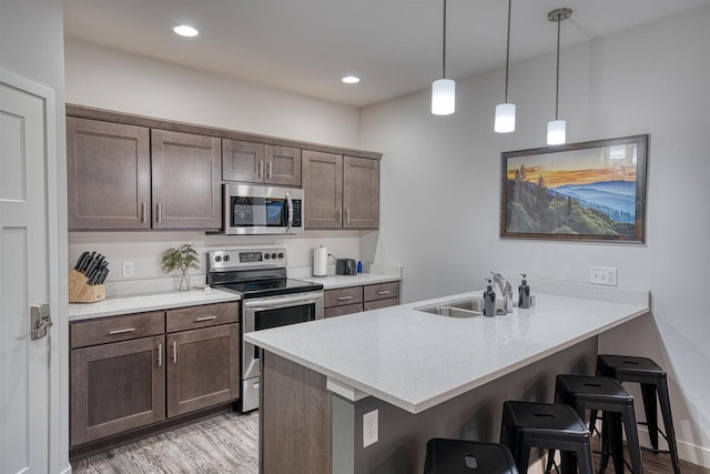 kitchen with a breakfast bar, a peninsula, a sink, stainless steel appliances, and dark brown cabinets