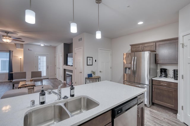 kitchen featuring light wood-style flooring, a sink, stainless steel appliances, a glass covered fireplace, and decorative light fixtures