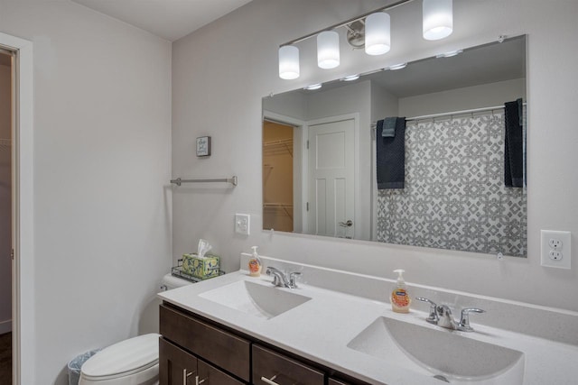 bathroom featuring double vanity, toilet, a walk in closet, and a sink