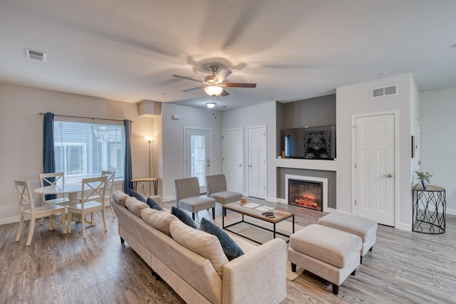 living room with visible vents, a warm lit fireplace, baseboards, and wood finished floors