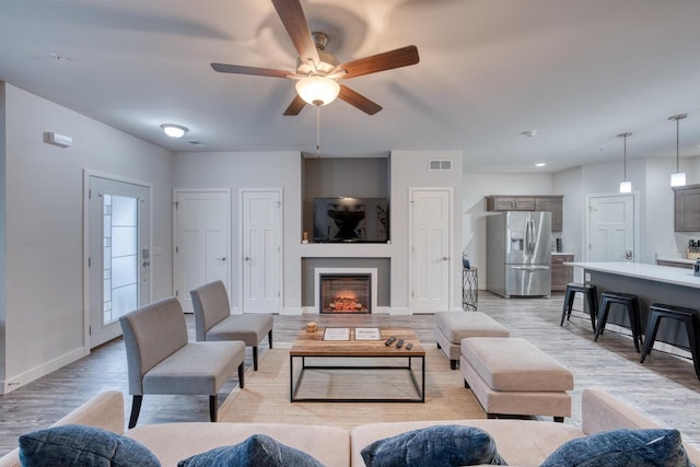 living area with light wood finished floors, visible vents, a lit fireplace, and baseboards