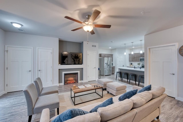 living area featuring visible vents, light wood-style flooring, baseboards, and a lit fireplace