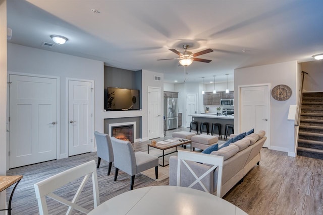 living room featuring baseboards, visible vents, light wood finished floors, a lit fireplace, and stairs