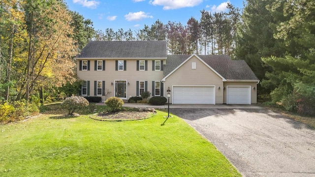 colonial home with a front yard, an attached garage, and aphalt driveway