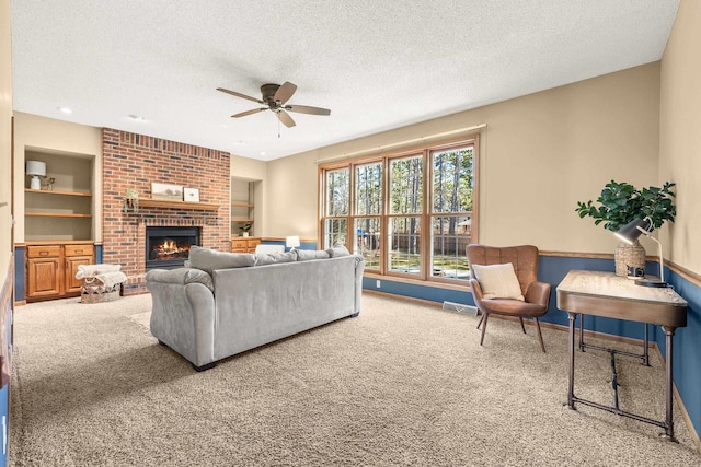 carpeted living area with built in features, a ceiling fan, baseboards, a fireplace, and a textured ceiling