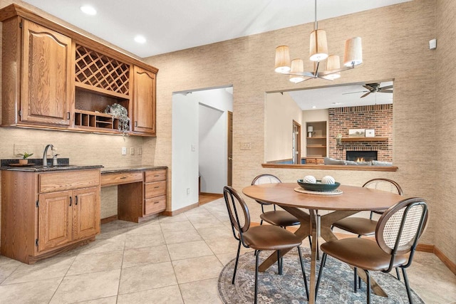 dining room with built in desk, light tile patterned floors, baseboards, a brick fireplace, and ceiling fan