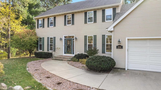 colonial home with a front lawn, a garage, and a shingled roof