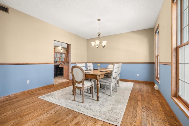 dining room with visible vents, a textured ceiling, wood finished floors, an inviting chandelier, and baseboards