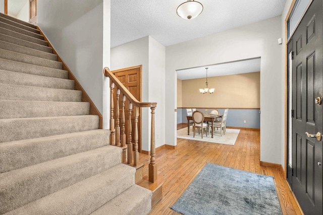 entryway with baseboards, a textured ceiling, light wood-style flooring, and stairs