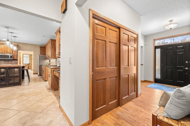 foyer entrance with light wood-type flooring, baseboards, and a textured ceiling