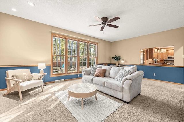 living area with visible vents, light carpet, a textured ceiling, baseboards, and ceiling fan