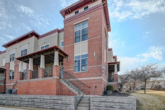 view of side of property with stairs, cooling unit, and brick siding