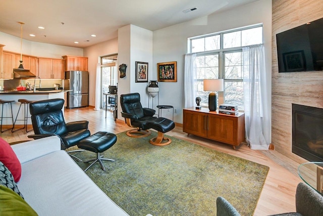 living room with a wealth of natural light, visible vents, a fireplace, and light wood-style floors