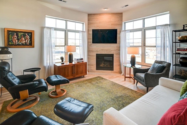 living room featuring wood finished floors, a healthy amount of sunlight, visible vents, and a large fireplace