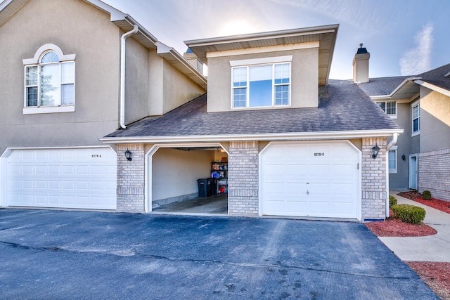 multi unit property featuring aphalt driveway, brick siding, roof with shingles, and stucco siding