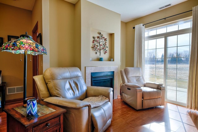 living area with a tiled fireplace, wood finished floors, and visible vents