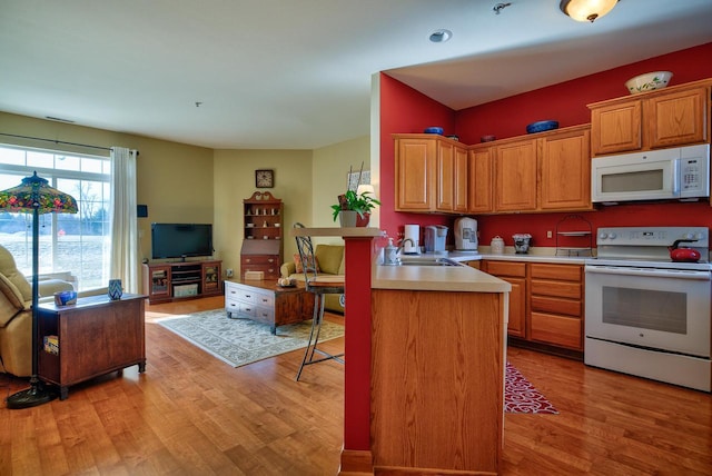 kitchen featuring light wood-type flooring, a sink, open floor plan, white appliances, and light countertops