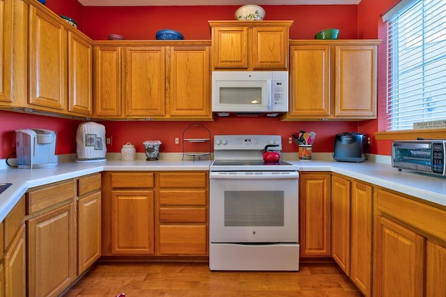 kitchen with a toaster, light countertops, light wood-style flooring, brown cabinets, and white appliances